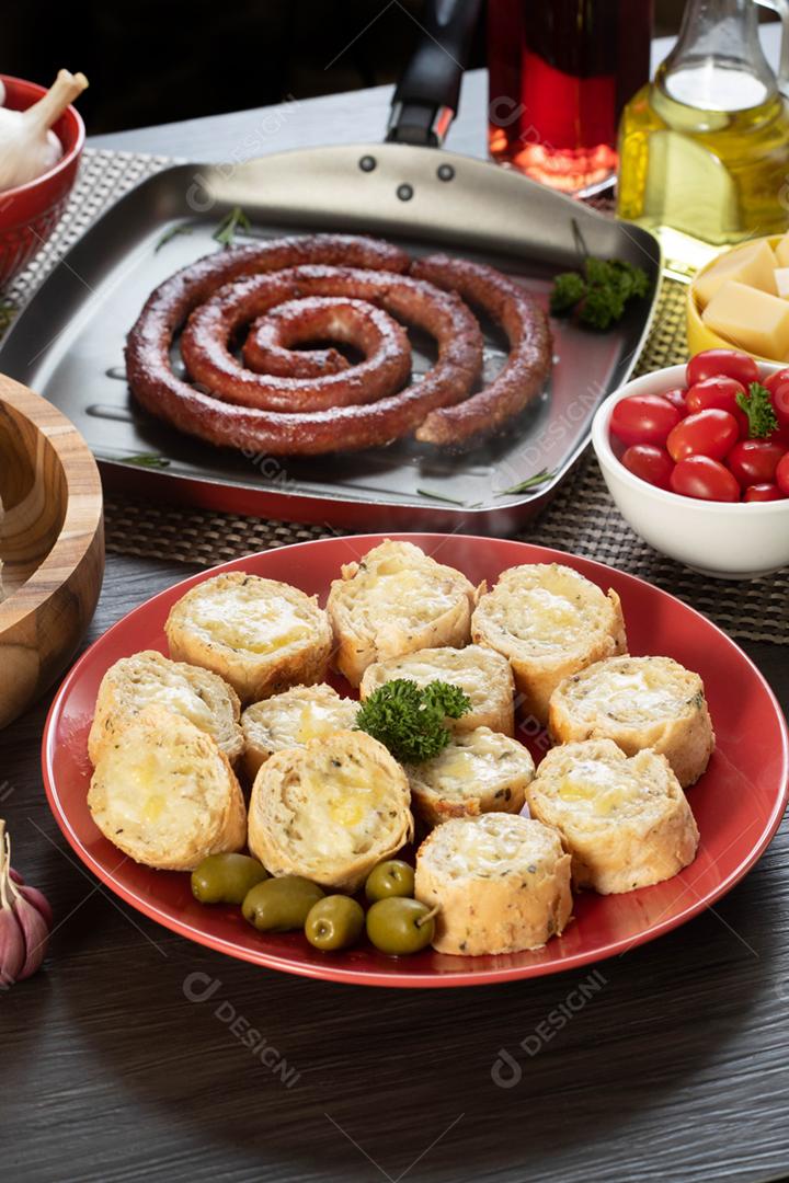 Pão de alho em um prato vermelho na mesa de churrasco com salsicha,