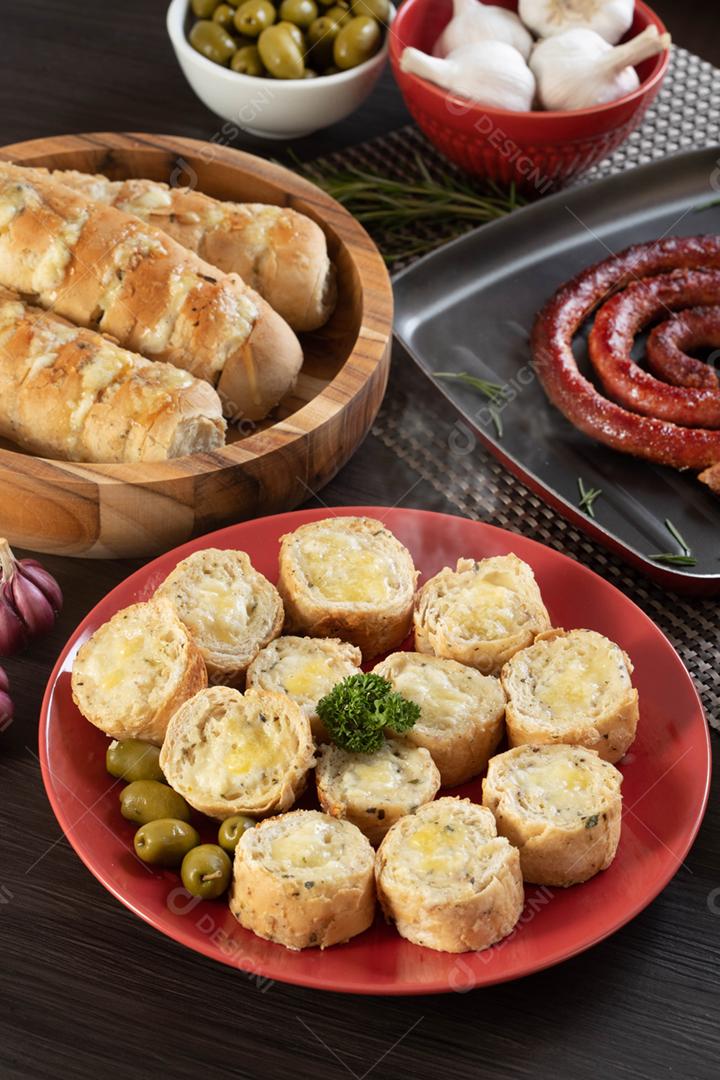 Pão de alho em um prato vermelho na mesa de churrasco com salsicha,