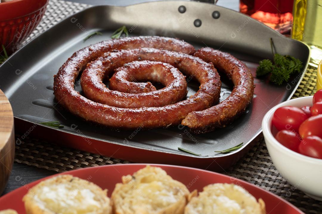 Linguiça assada com pão de salsicha e alho em um prato vermelho na mesa de churrasco wi
