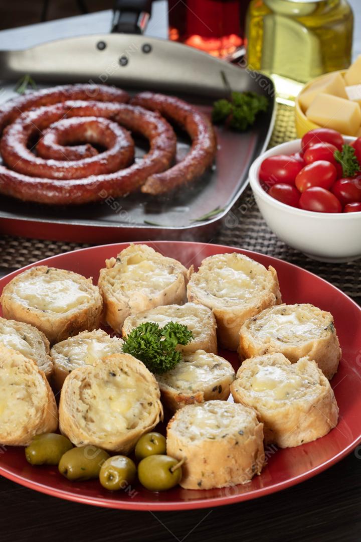 Pão de alho em um prato vermelho na mesa de churrasco com salsicha,