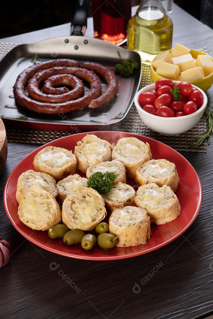 Pão de alho em um prato vermelho na mesa de churrasco com salsicha,