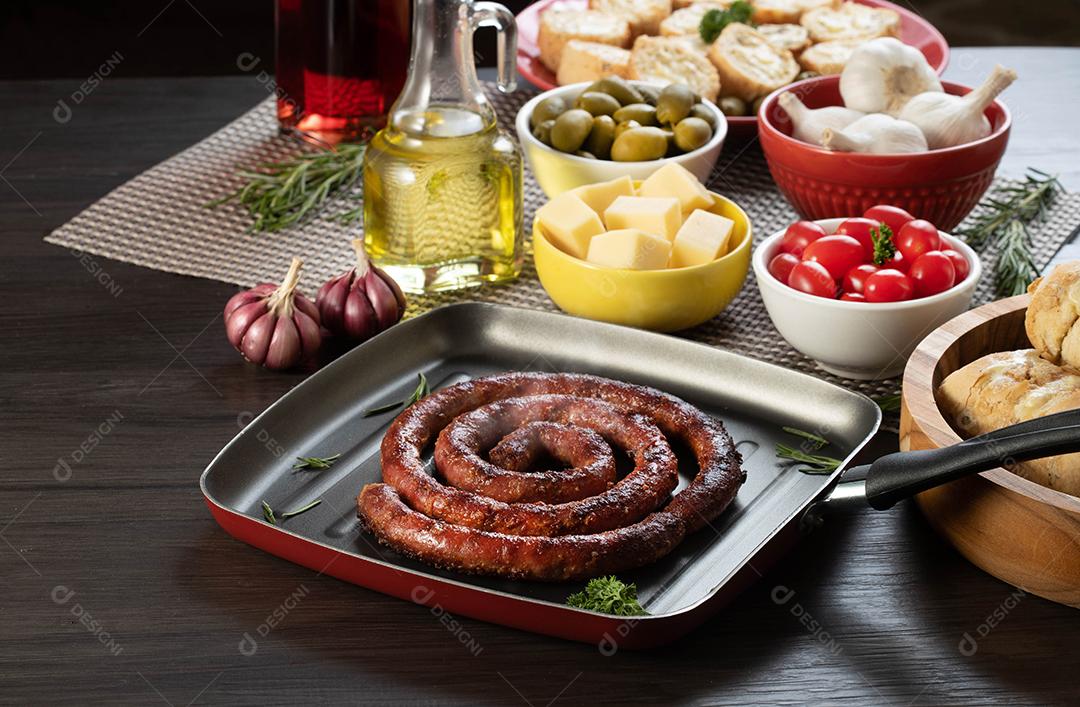 Pão de salsicha e alho em um prato vermelho na mesa de churrasco com aperitivos, queijo, alecrim, azeitonas e tomate cereja