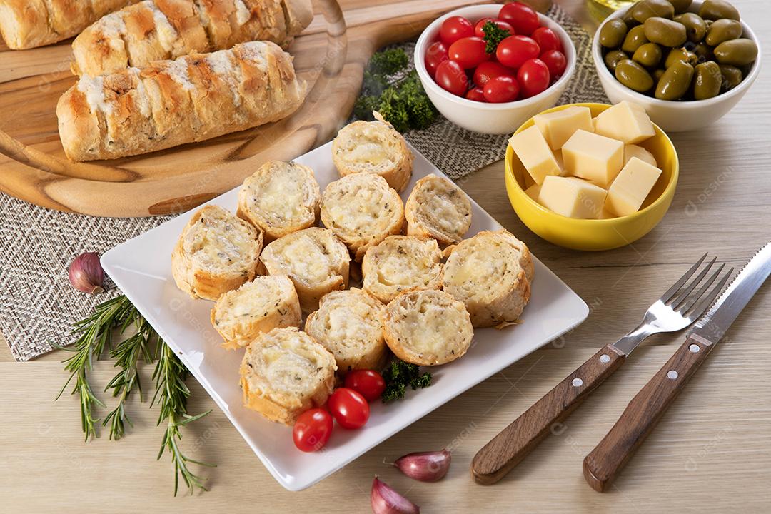 Pão de alho em prato quadrado branco em cima da mesa com queijo, alecrim, azeitonas e tomate cereja