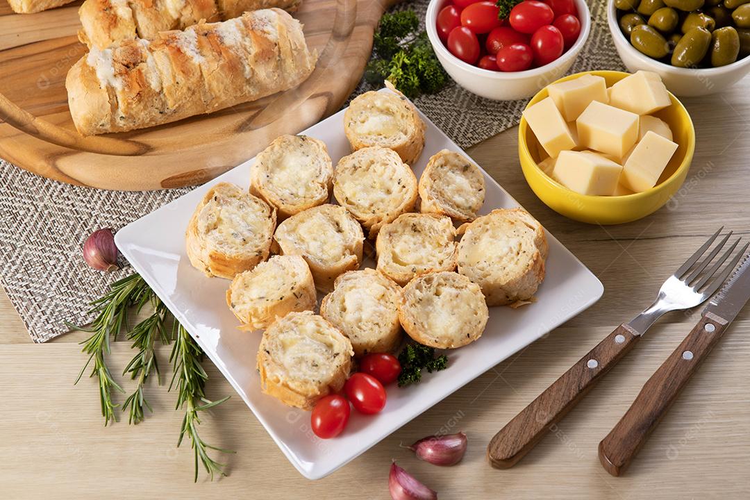 Pão de alho em prato quadrado branco em cima da mesa com queijo, alecrim, azeitonas e tomate cereja