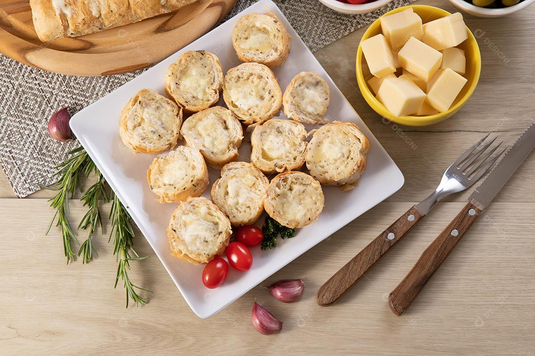 Pão de alho em prato quadrado branco em cima da mesa com queijo, alecrim, azeitonas e tomate cereja