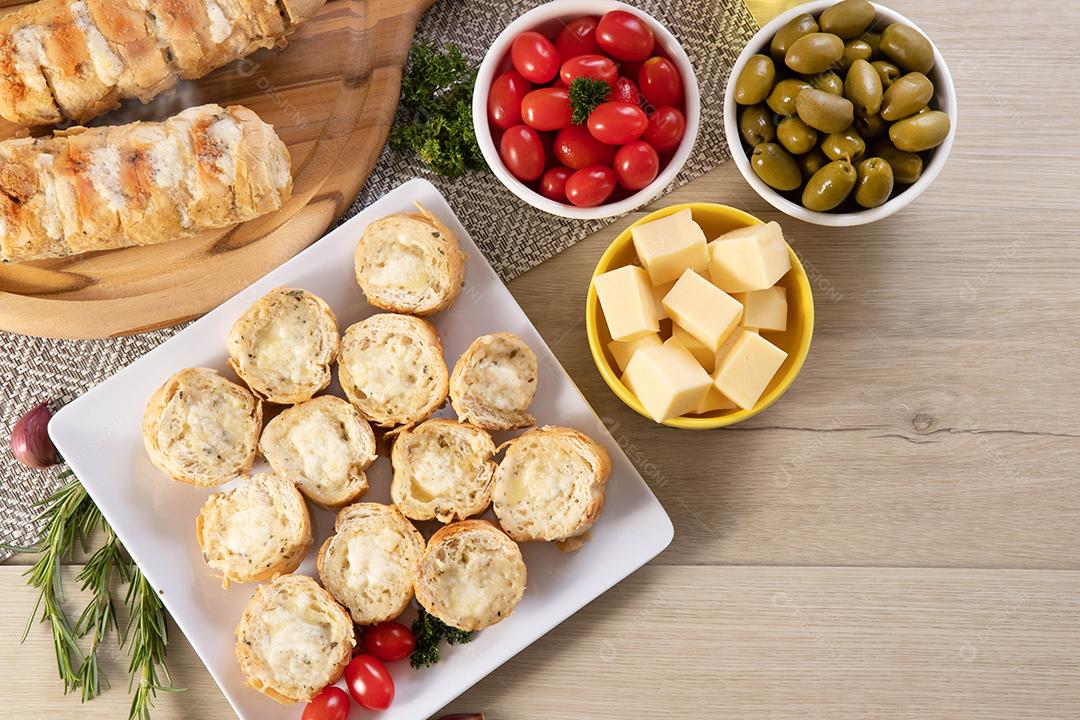 Pão de alho em prato quadrado branco em cima da mesa com queijo, alecrim, azeitonas e tomate cereja