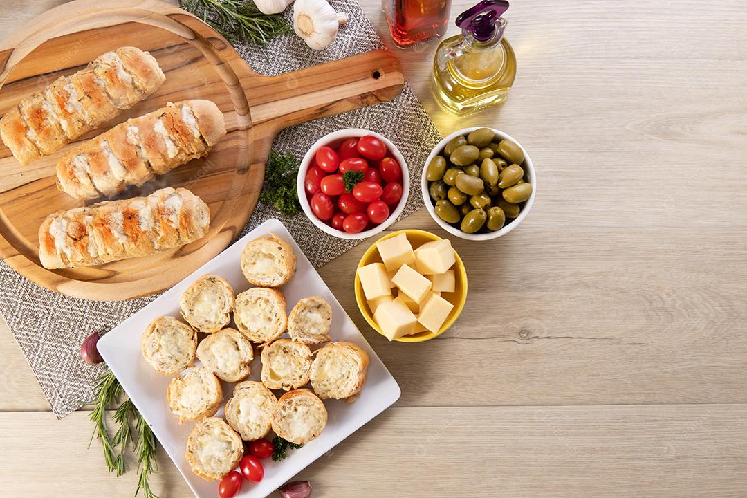 Pão de alho em prato quadrado branco em cima da mesa com queijo, alecrim, azeitonas e tomate cereja
