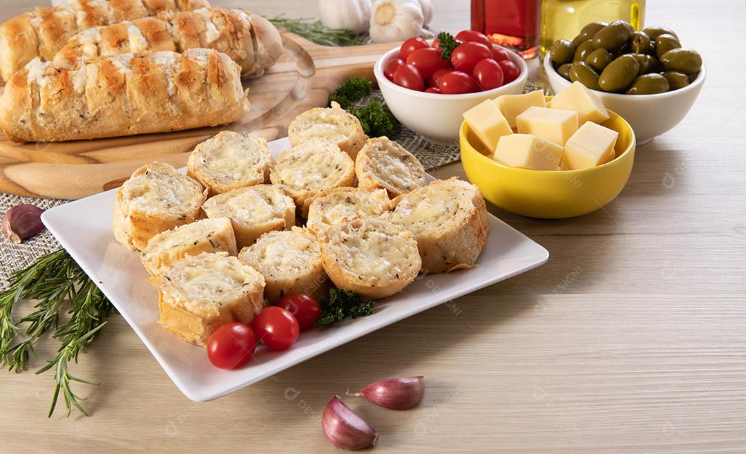 Pão de alho em prato quadrado branco em cima da mesa com queijo, alecrim, azeitonas e tomate cereja