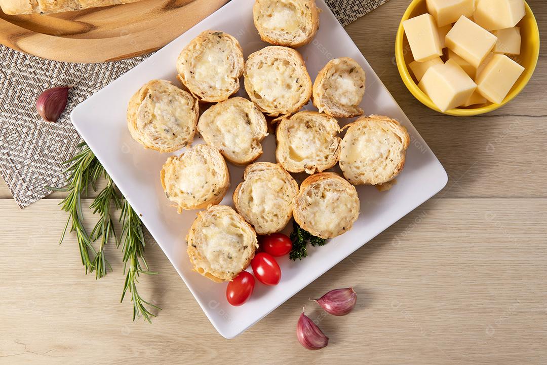 Pão de alho em prato quadrado branco em cima da mesa com queijo, alecrim, azeitonas e tomate cereja
