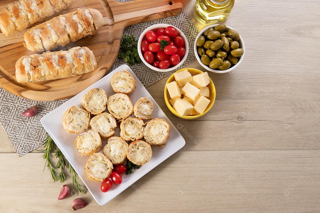 Pão de alho em prato quadrado branco em cima da mesa com queijo, alecrim, azeitonas e tomate cereja