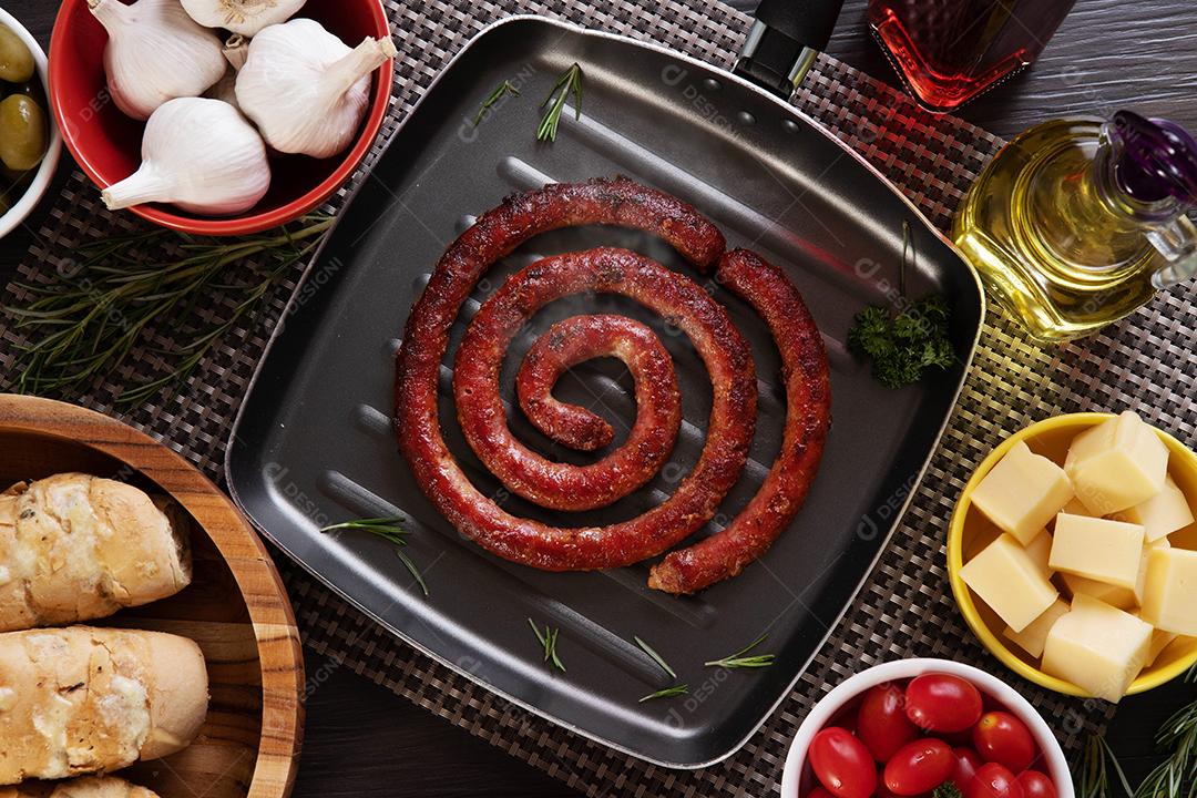 Sausage and garlic bread on a red plate on the barbecue table with appetizers, cheese, rosemary, olives and cherry tomatoes