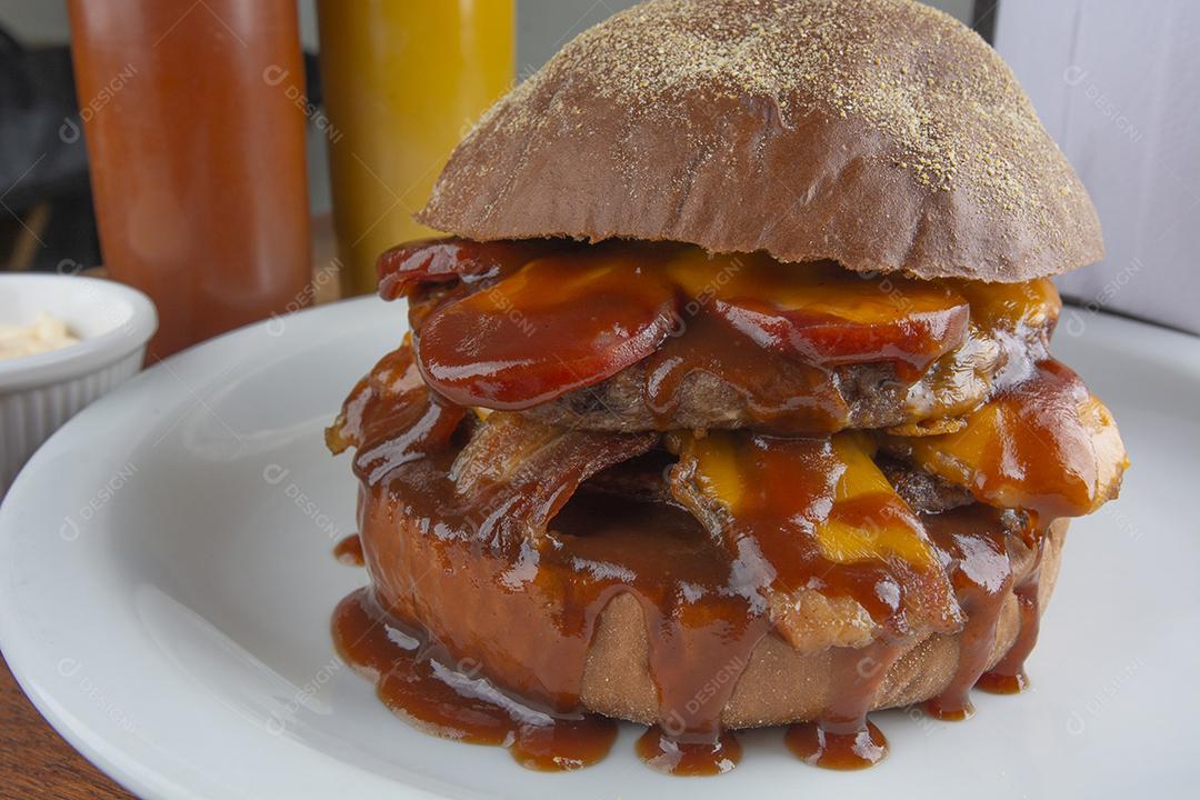 Cheeseburger duplo com molho barbecue sobre chapa branca.