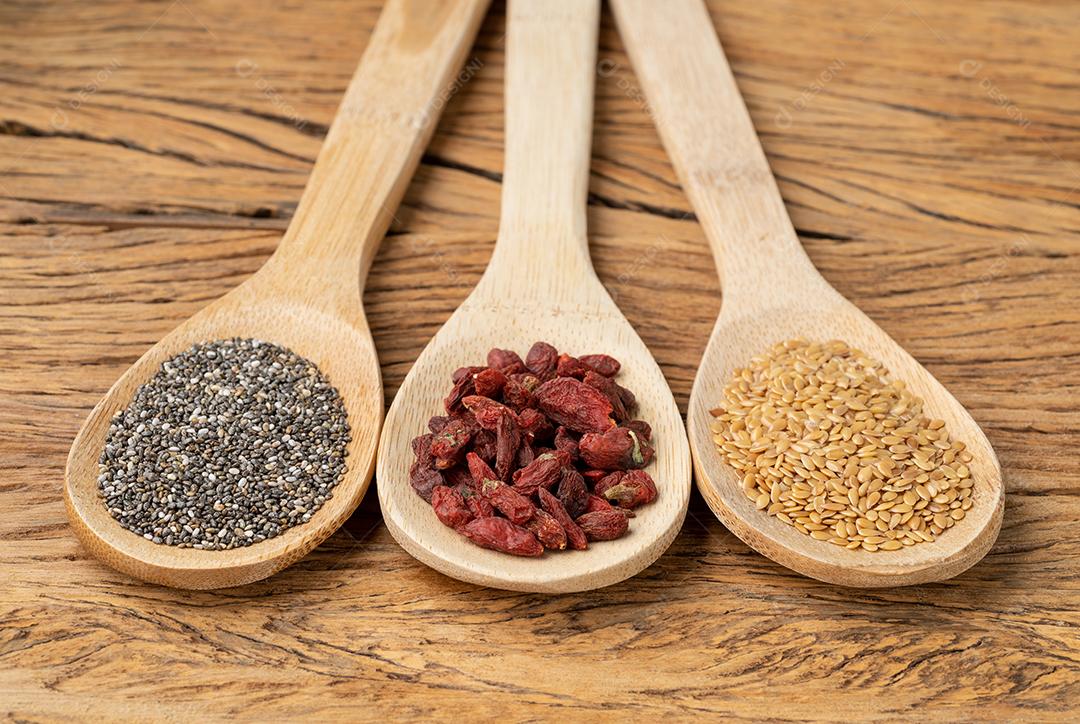 Super alimentos variados em colheres sobre a mesa de madeira. Chia, linhaça e goji berry.