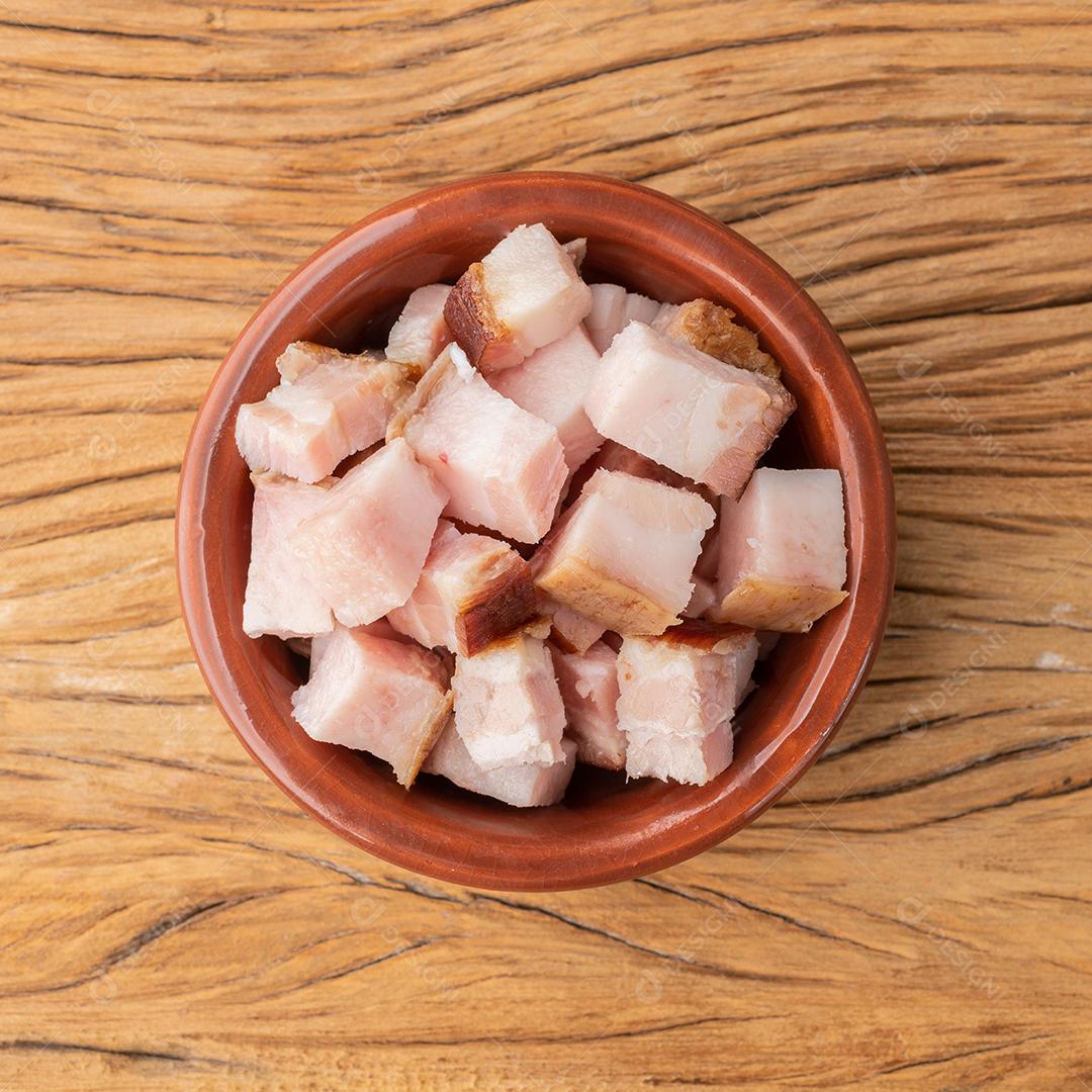 Cubos de bacon defumado em uma tigela sobre a placa de madeira.