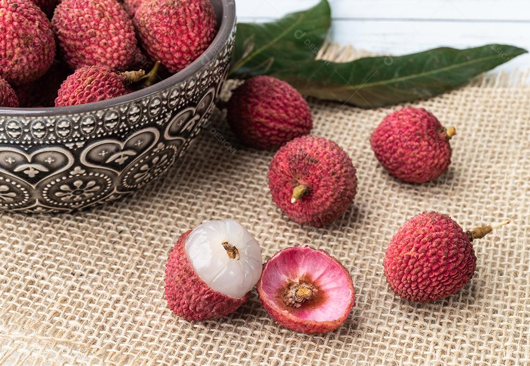 Lichias em uma tigela com frutas cortadas sobre a mesa de madeira.