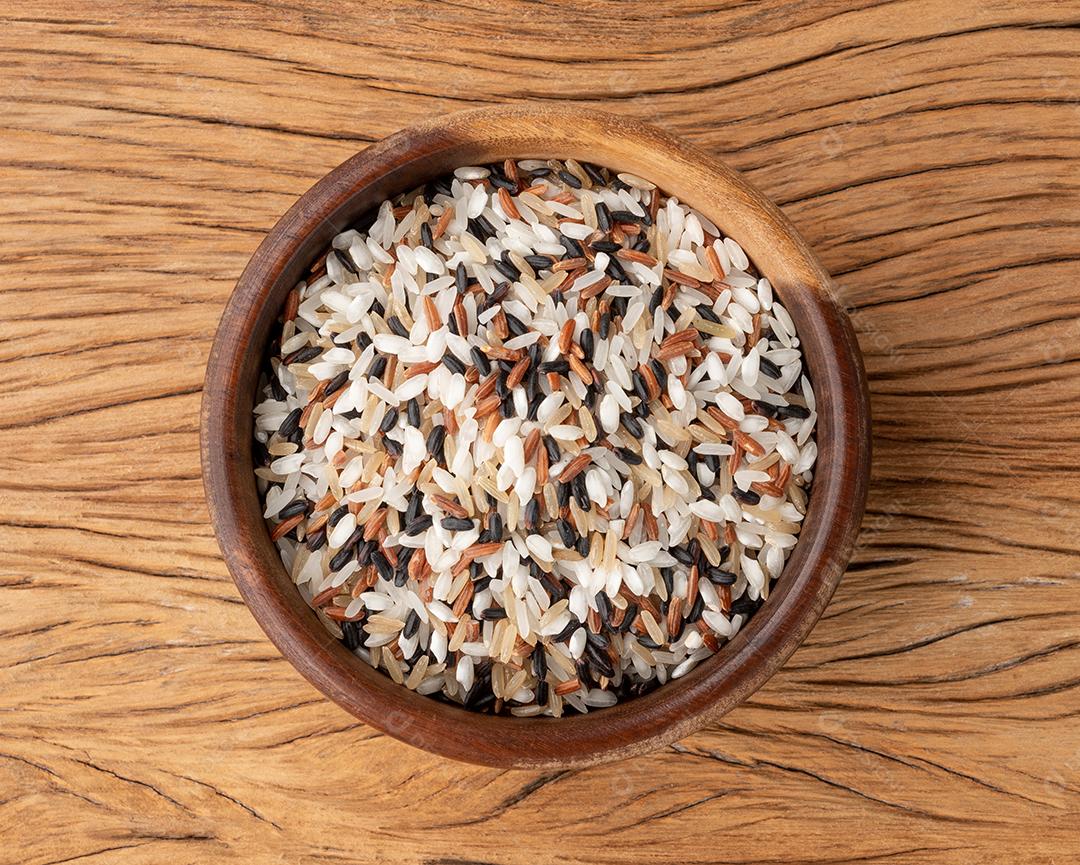 Arroz sortido cru em uma tigela sobre a mesa de madeira.