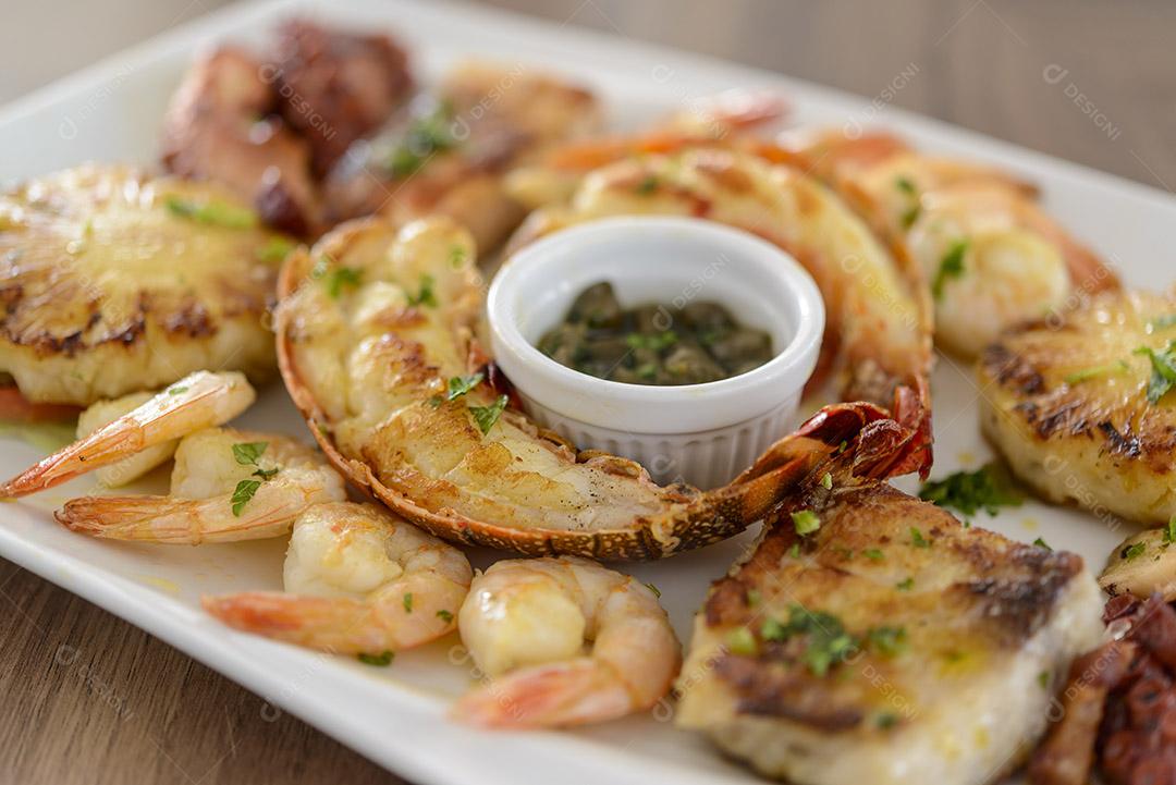 Frutos do mar. Lagosta, camarão, polvo e peixe em tigela branca na mesa de madeira. comida brasileira.
