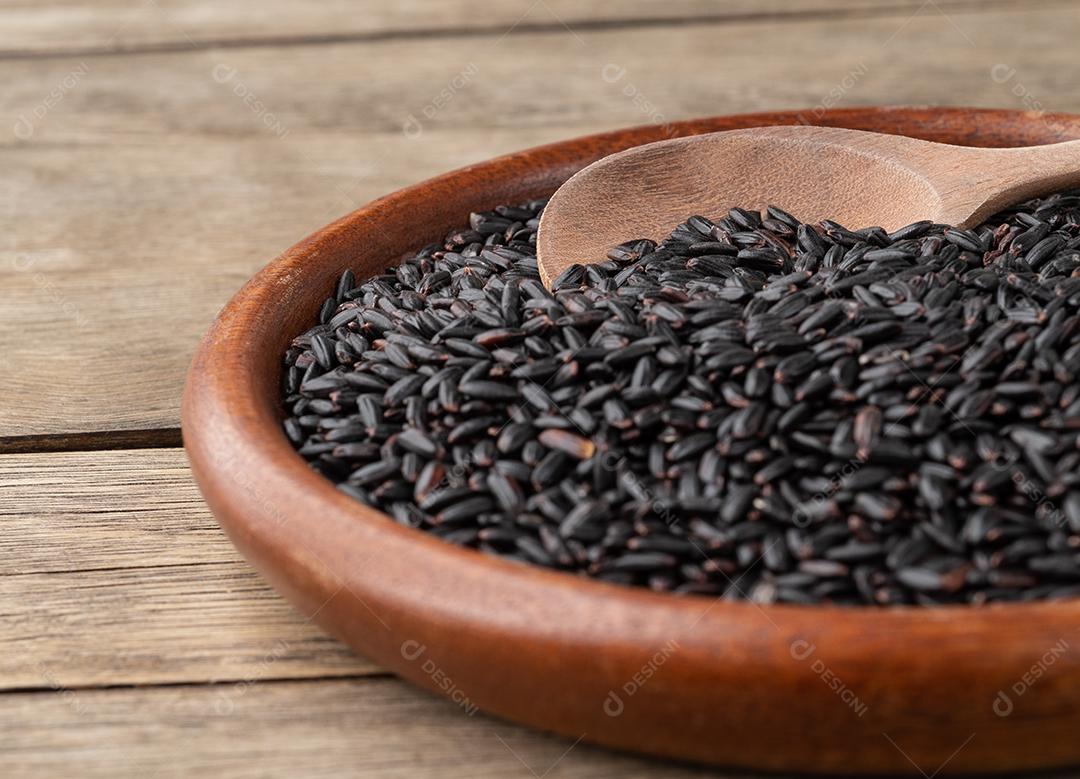 Foco estreito, arroz preto cru em um prato sobre a mesa de madeira.