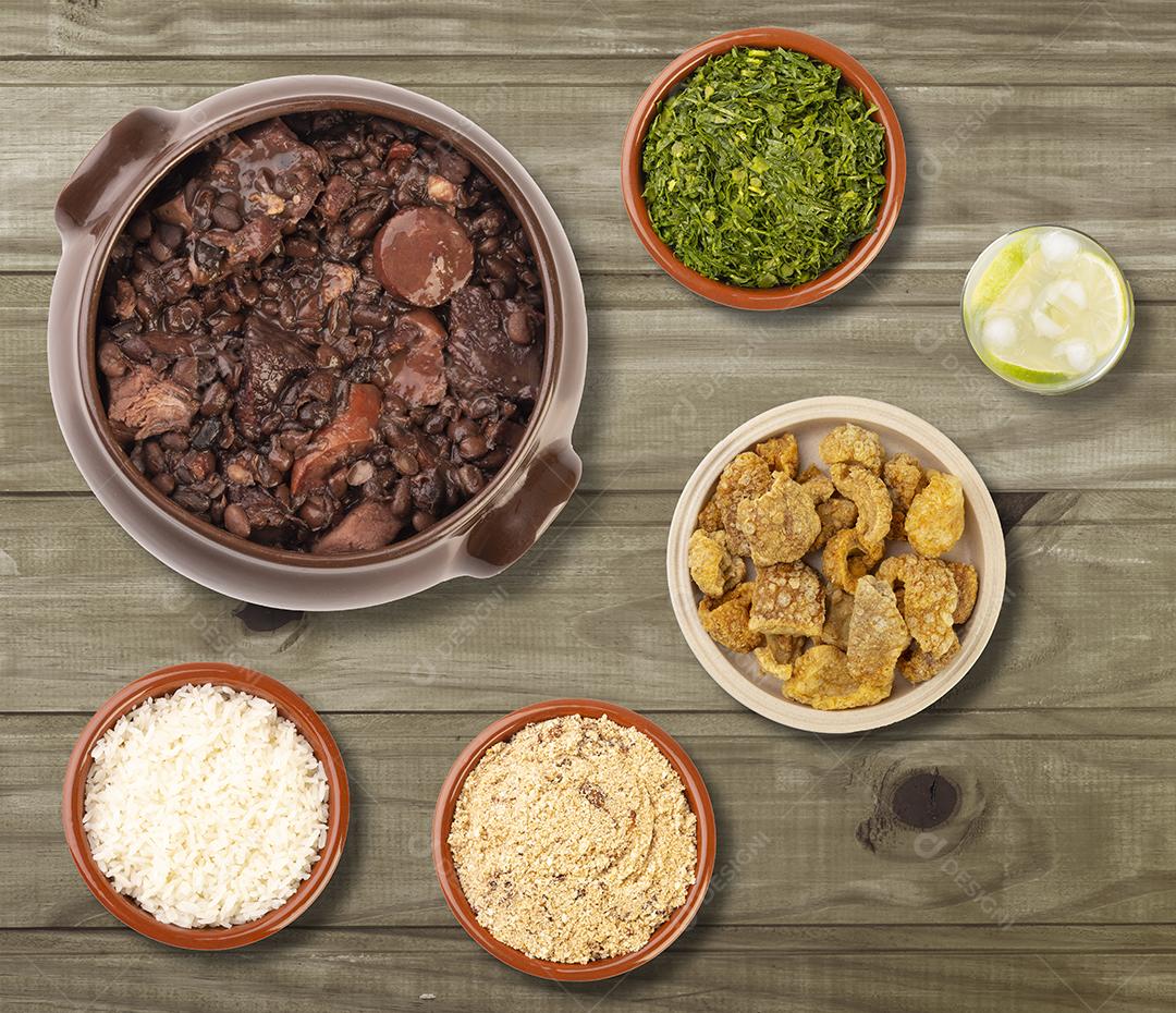 Feijoada brasileira típica com caipirinha e acompanhamentos sobre mesa de madeira