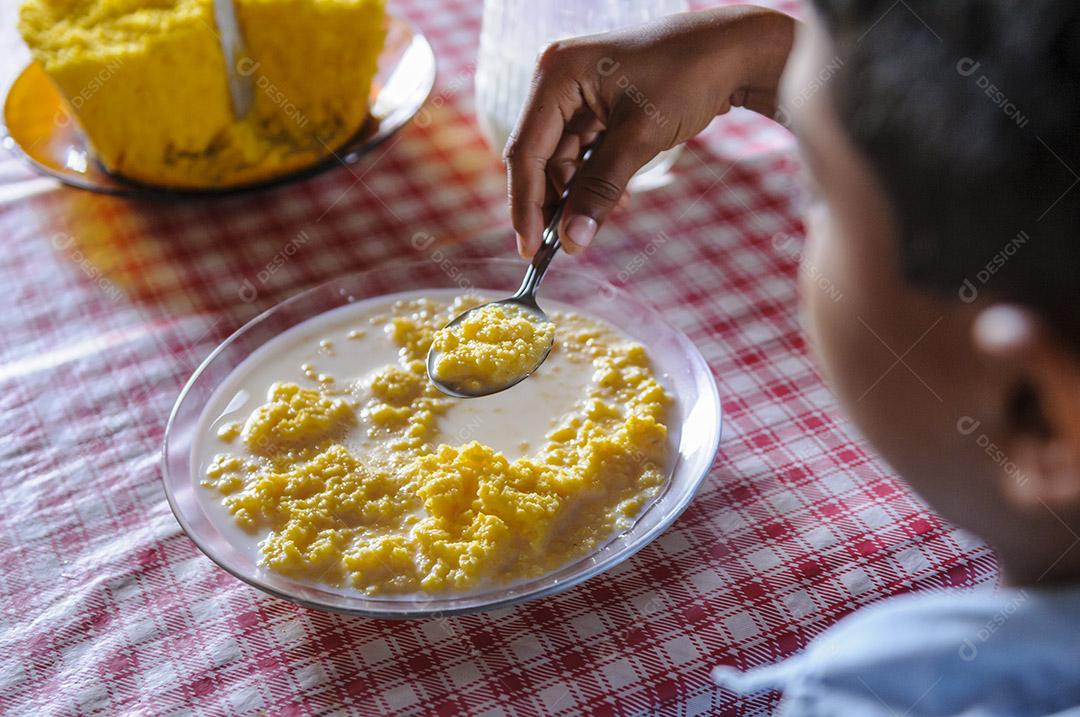 Criança brasileira comendo cuscuz de milho com leite.