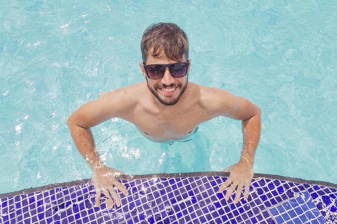 Homem bonito sorrindo na piscina na paisagem de verão