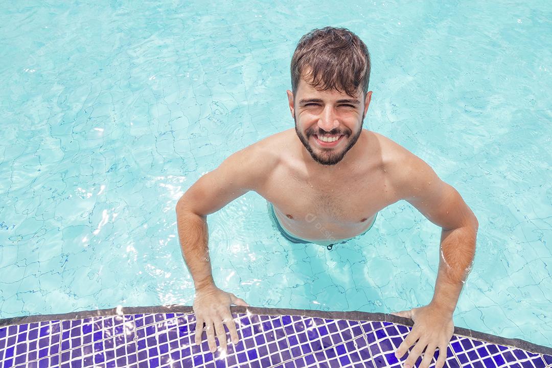 Homem bonito sorrindo na piscina na paisagem de verão