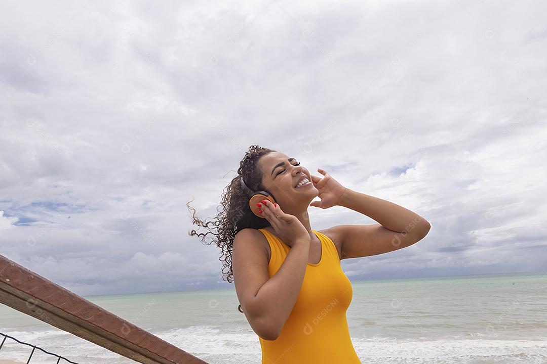 Férias de verão, tecnologia e conceito de internet. mulher afro ouvindo música com fone de ouvido na praia