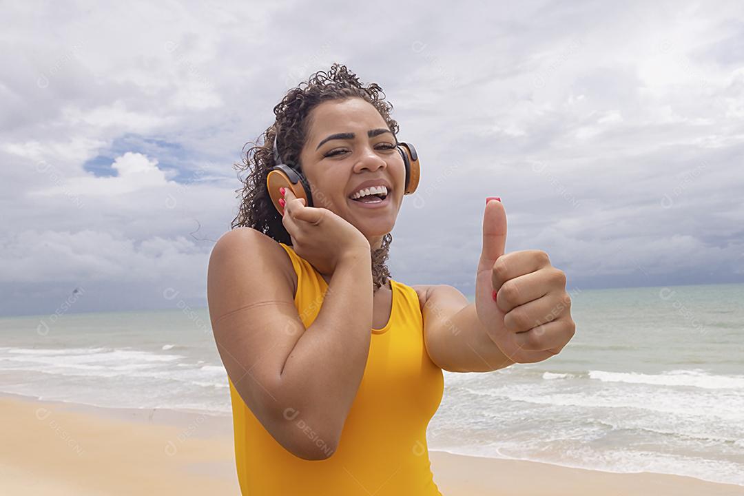 Férias de verão, tecnologia e conceito de internet. mulher afro ouvindo música com fone de ouvido na praia