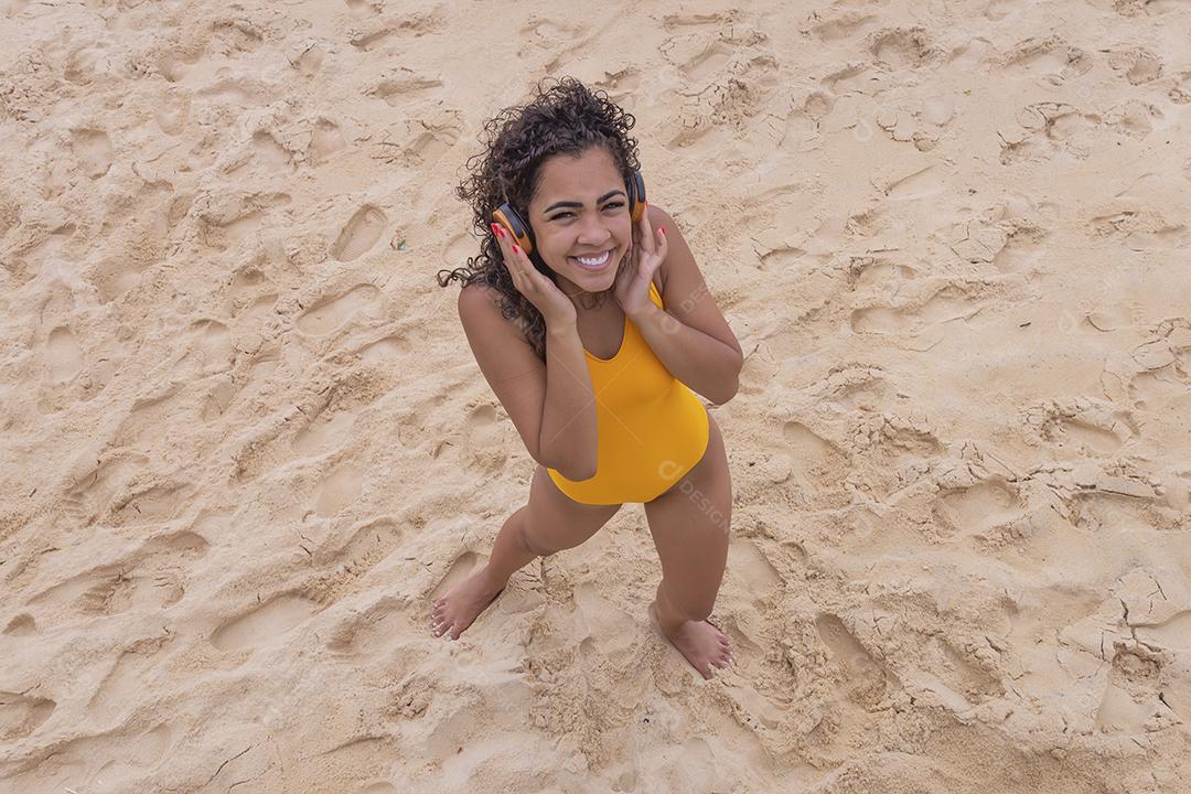 Férias de verão, tecnologia e conceito de internet. mulher afro ouvindo música com fone de ouvido na praia