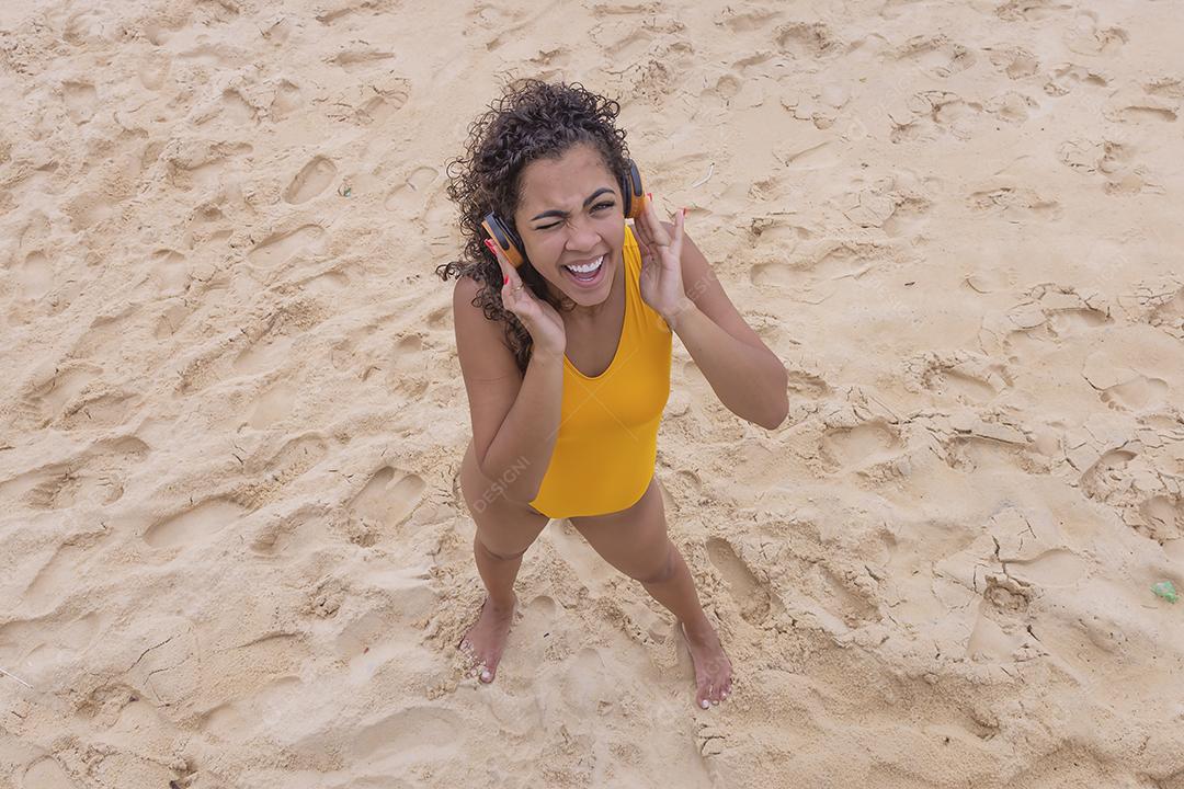 Férias de verão, tecnologia e conceito de internet. mulher afro ouvindo música com fone de ouvido na praia