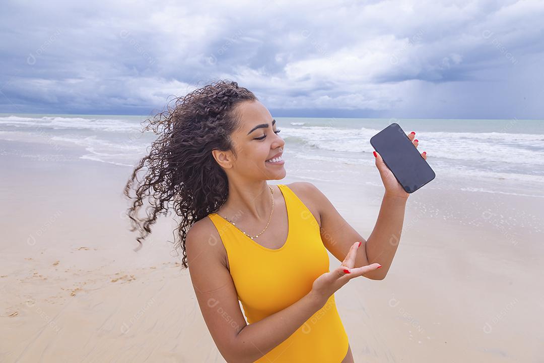 férias de verão, tecnologia e conceito de internet. Mulher afro com celular com tela em branco na praia