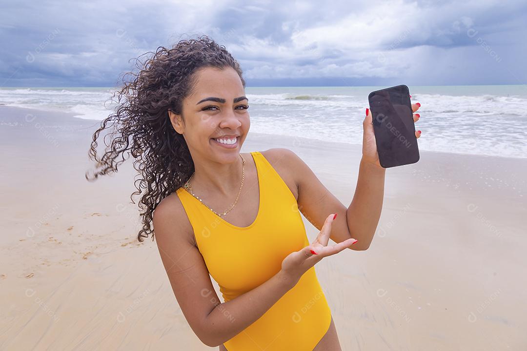 férias de verão, tecnologia e conceito de internet. Mulher afro com celular com tela em branco na praia
