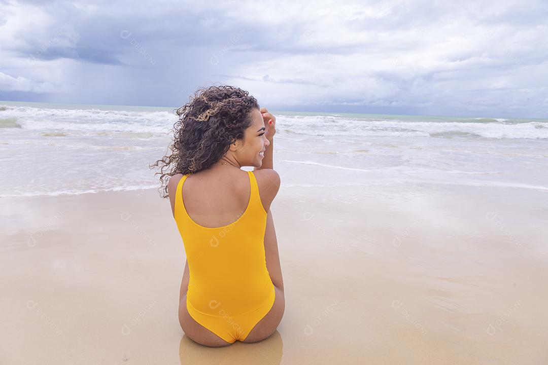 Mulher jovem na praia. Mulher afro sentada na areia da praia em um lindo dia de verão.