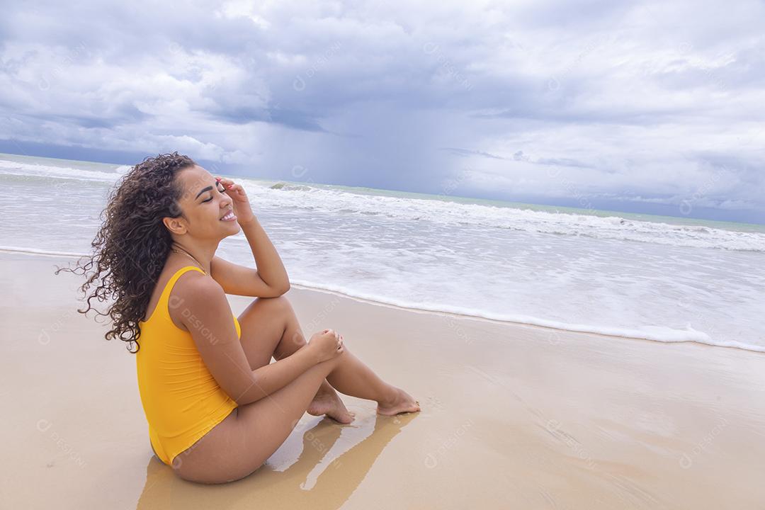 Mulher jovem na praia. Mulher afro sentada na areia da praia em um lindo dia de verão.