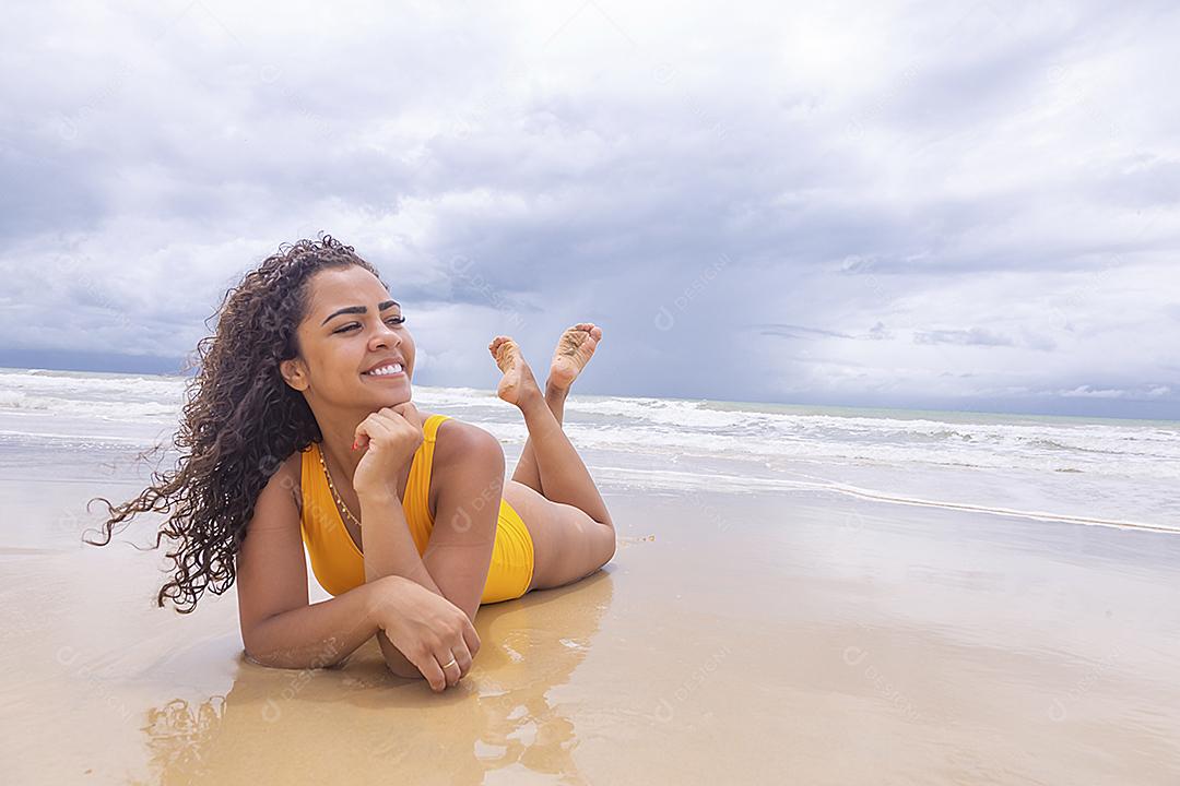 Mulher jovem na praia. Mulher afro sentada na areia da praia em um lindo dia de verão.