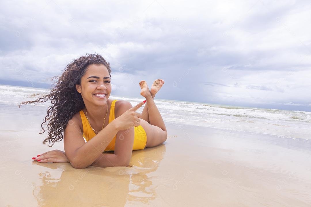 Mulher jovem na praia. Mulher afro sentada na areia da praia em um lindo dia de verão.