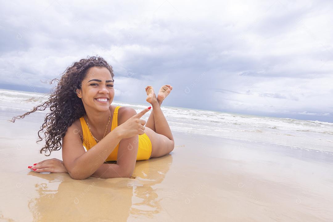 Mulher jovem na praia. Mulher afro sentada na areia da praia em um lindo dia de verão.