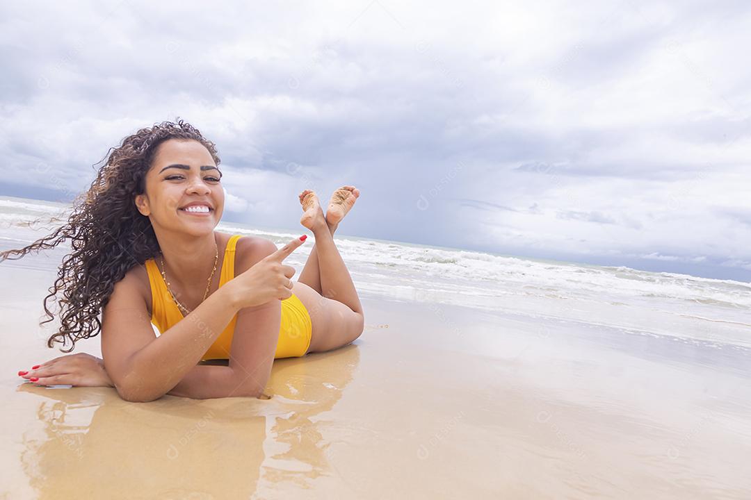 Mulher jovem na praia. Mulher afro sentada na areia da praia em um lindo dia de verão.