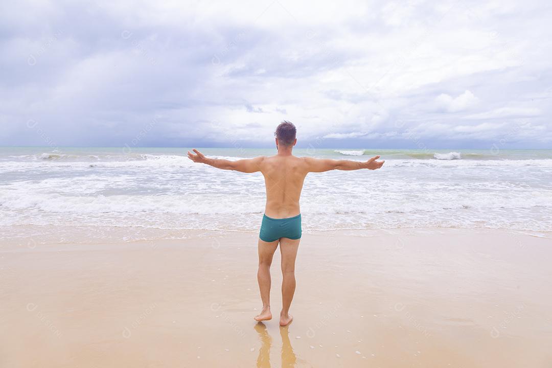 Menino olhando para o mar de costas com os braços estendidos