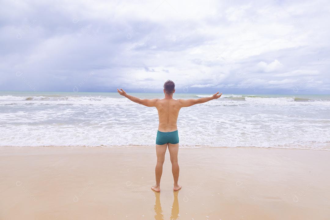 Menino olhando para o mar de costas com os braços estendidos