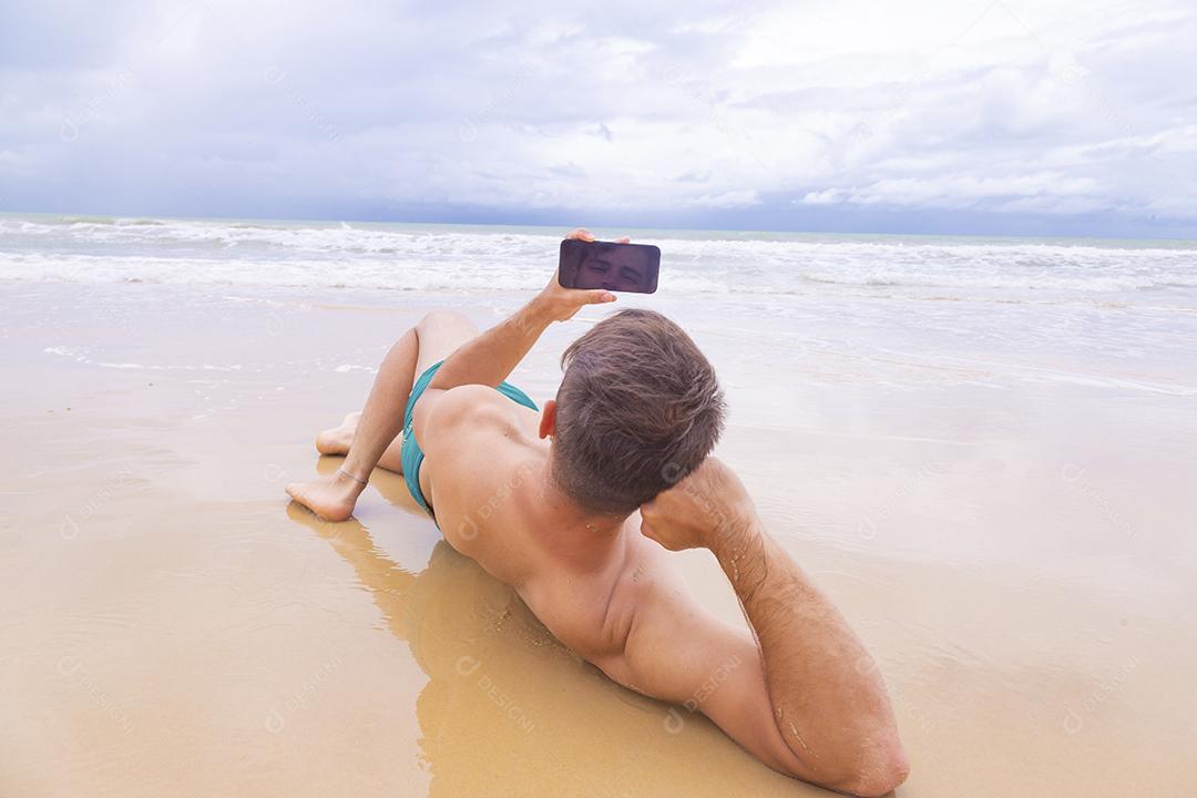 Rapaz olhando para a tela do celular em branco com espaço de cópia na areia da praia. Feriado