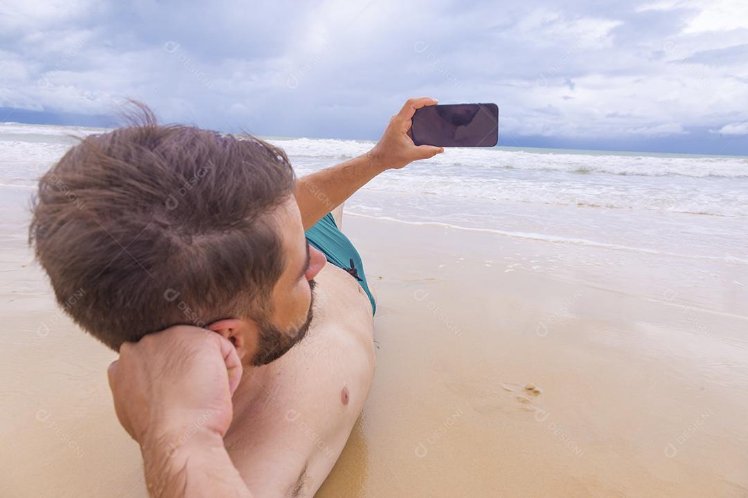 Rapaz olhando para a tela do celular em branco com espaço de cópia na areia da praia. Feriado