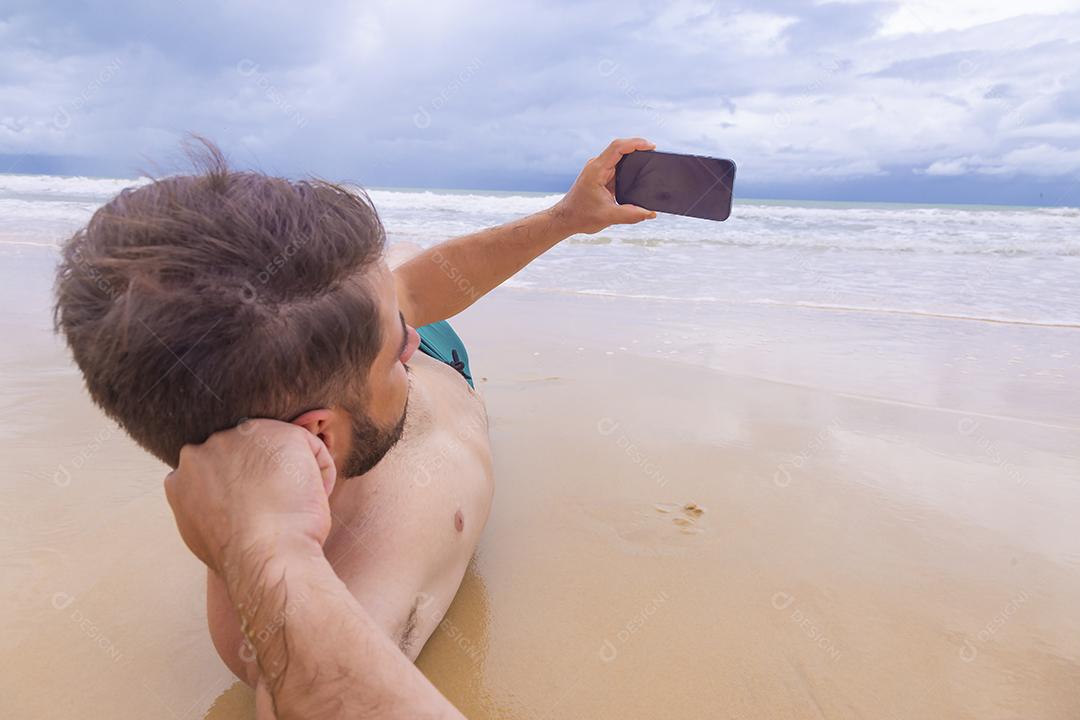 Rapaz olhando para a tela do celular em branco com espaço de cópia na areia da praia. Feriado