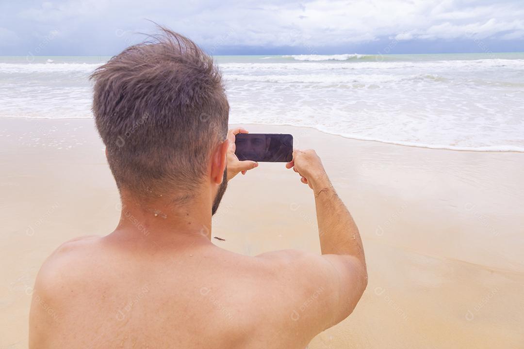 Rapaz olhando para a tela do celular em branco com espaço de cópia na areia da praia. Feriado