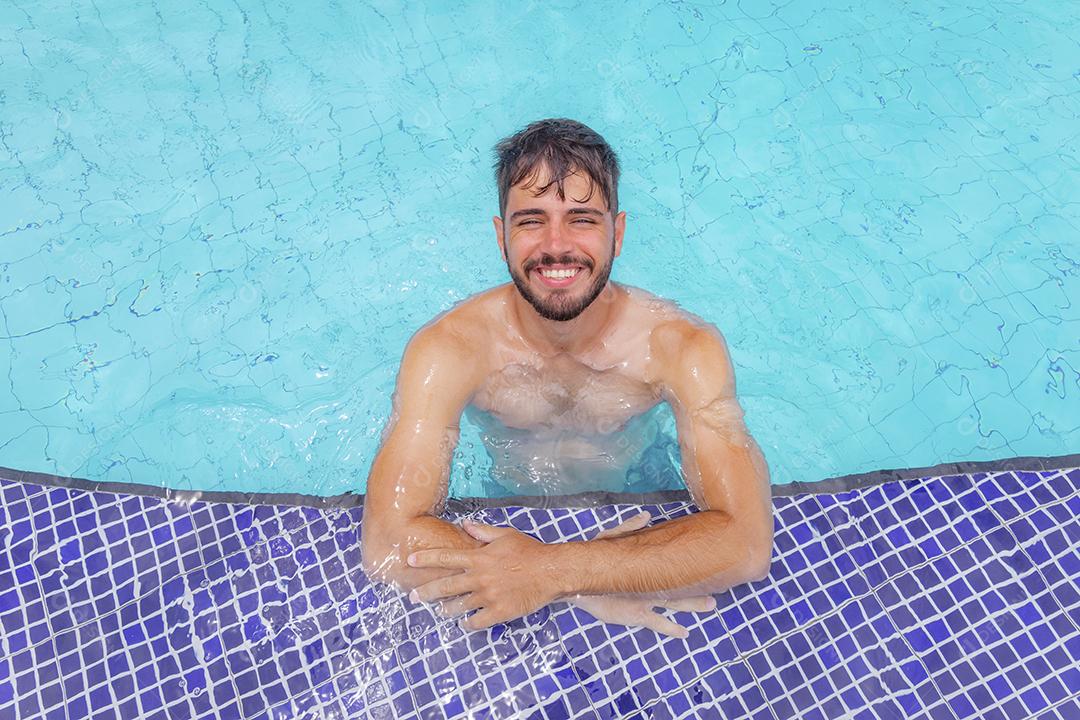 Homem bonito sorrindo na piscina na paisagem de verão