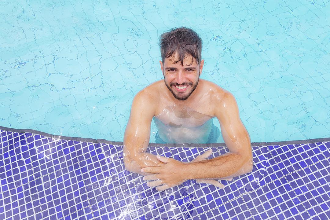 Homem bonito sorrindo na piscina na paisagem de verão