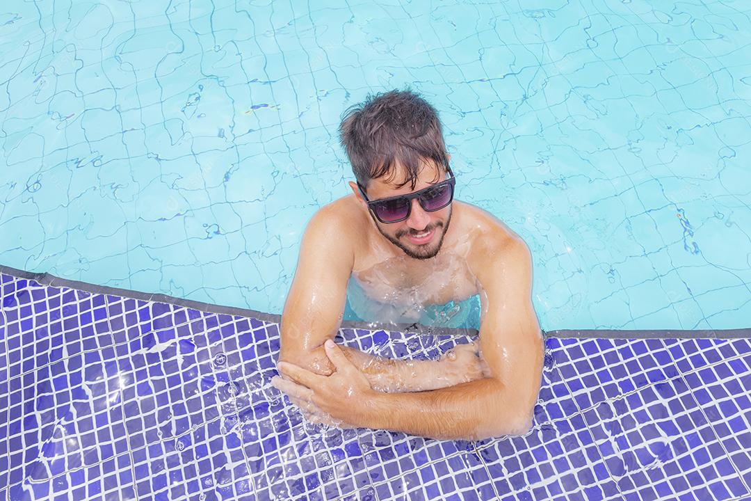 Homem bonito sorrindo na piscina na paisagem de verão