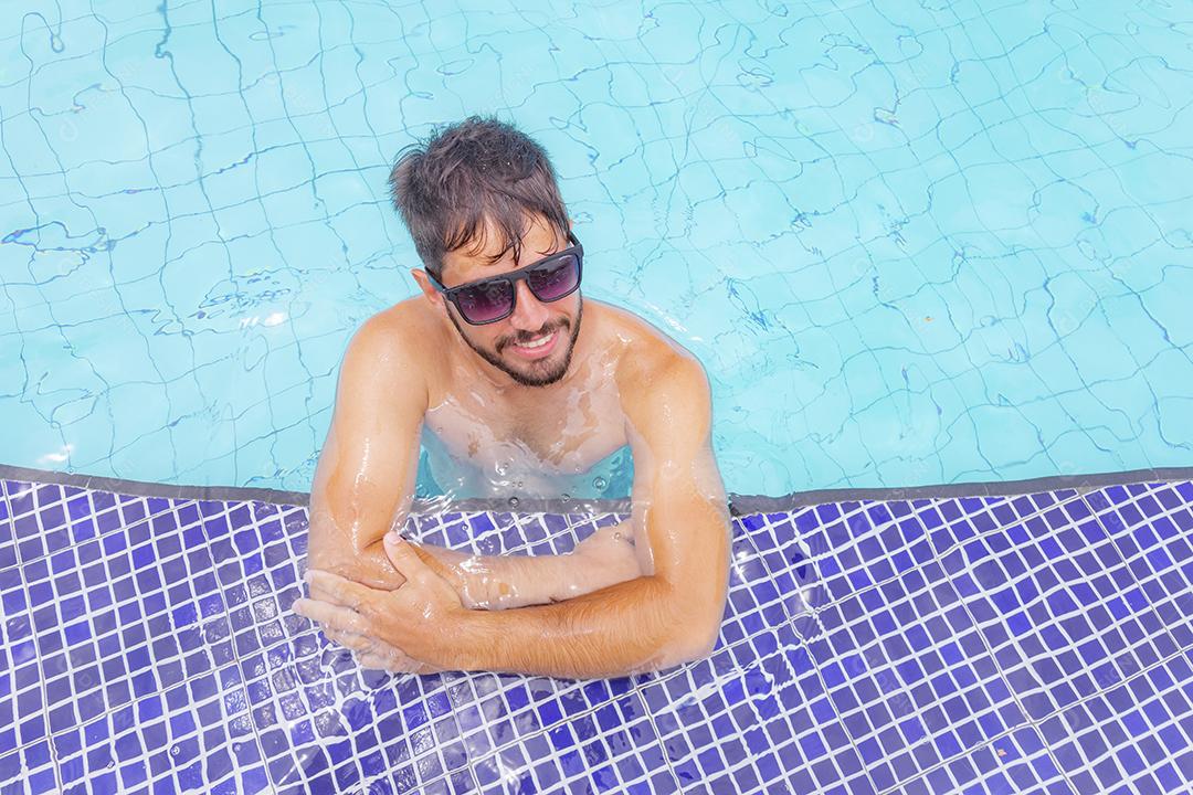 Homem bonito sorrindo na piscina na paisagem de verão