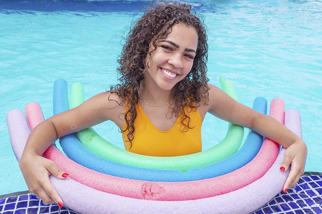 Jovem afro de férias aproveitando a piscina do hotel usando bóias flutuantes