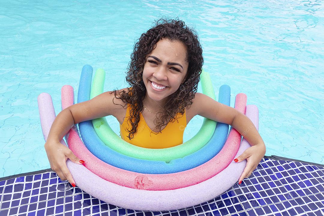 Jovem afro de férias aproveitando a piscina do hotel usando bóias flutuantes